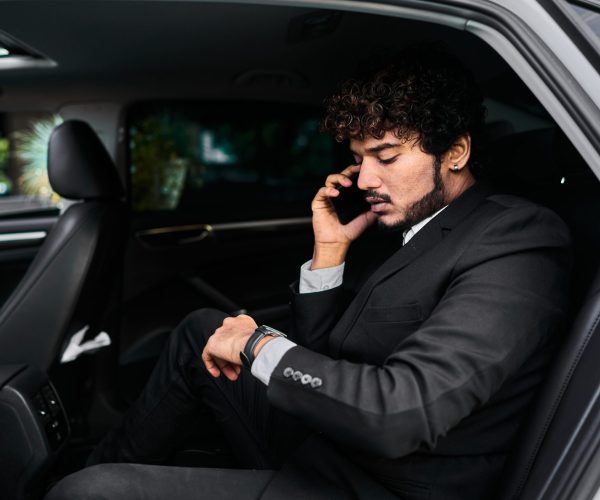 Curly-haired businessman in the backseat talking on the phone.